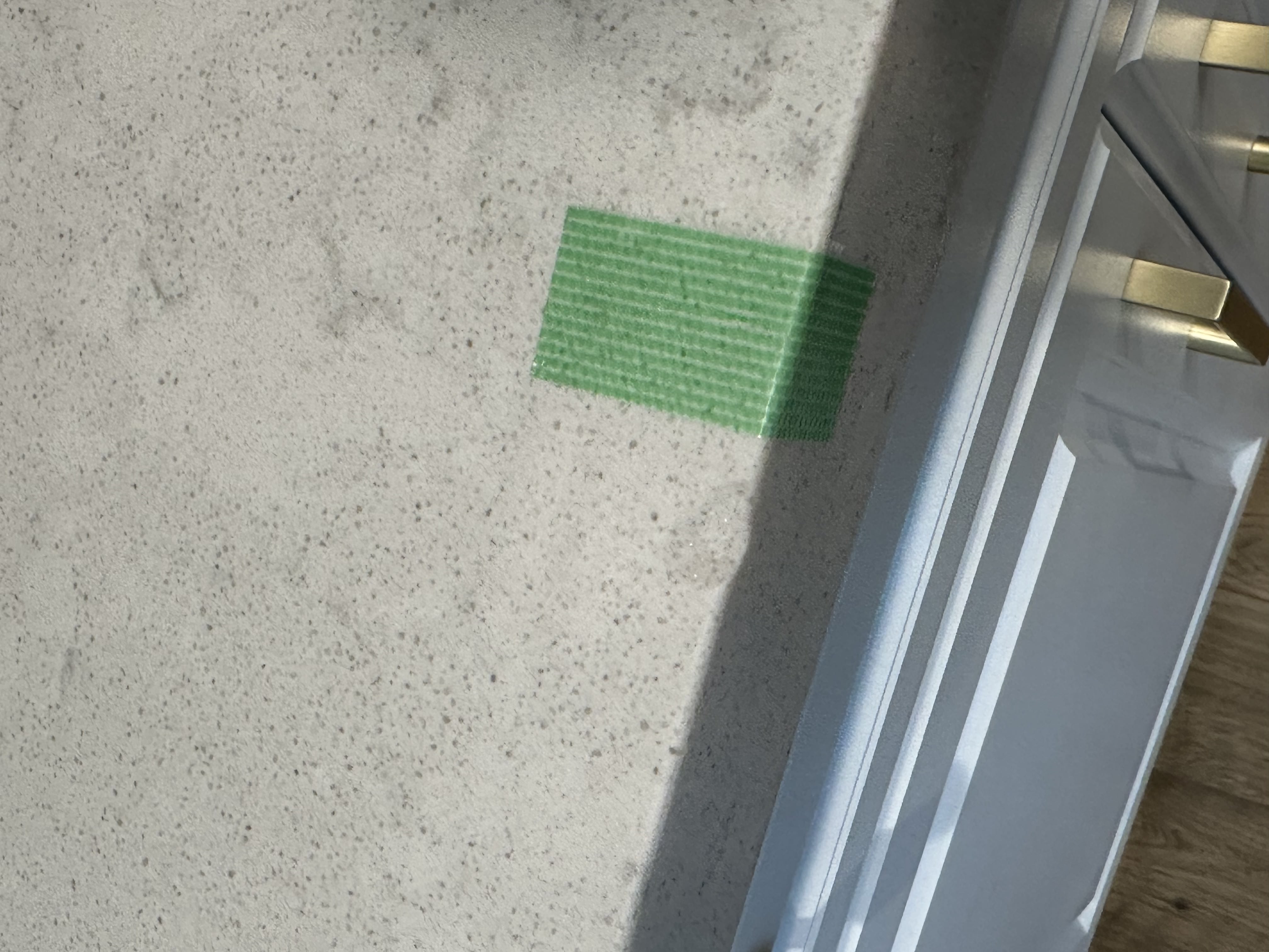 Chip on a speckled quartz countertop edge marked before repair